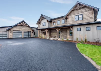 Modern rustic two-story house with wood siding, attached garage, large driveway, and minimal landscaping.