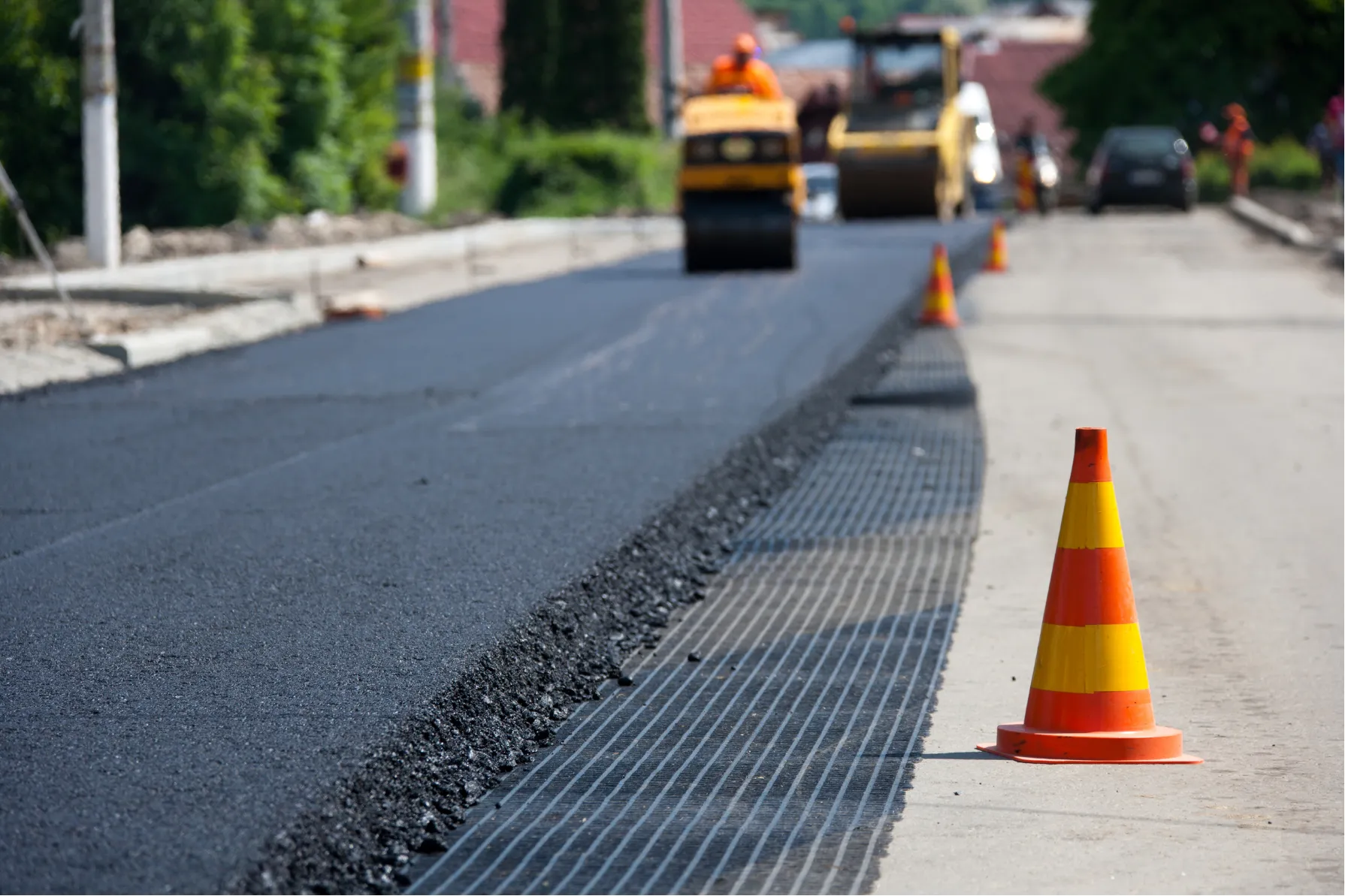 Fresh asphalt being laid on a road, with traffic cones marking the construction area.