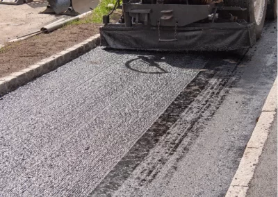 A paving machine lays fresh asphalt on a road during street construction.