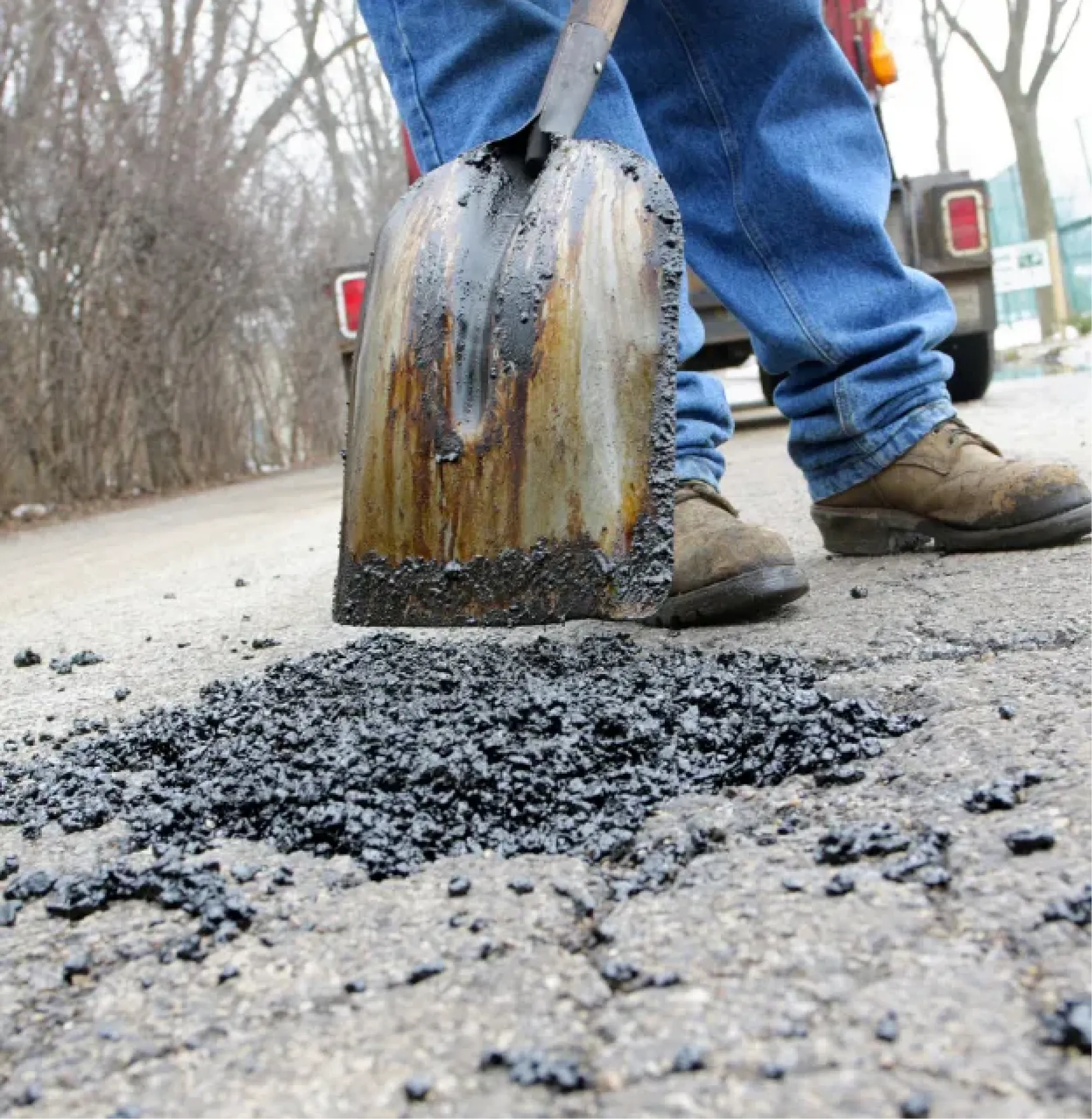 Close-up of a person shoveling asphalt to fill a pothole on a cracked road.