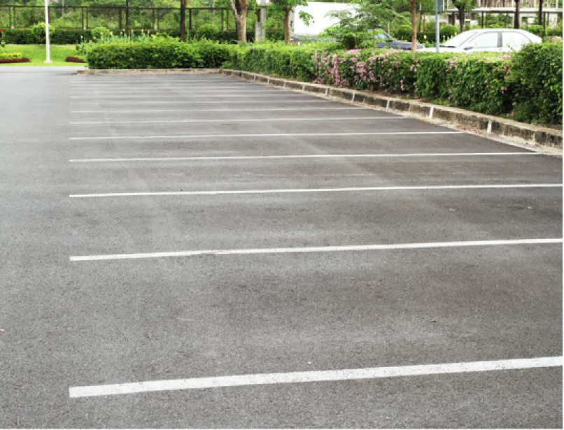 Freshly paved black asphalt driveway in a suburban neighborhood with green lawns and trees.