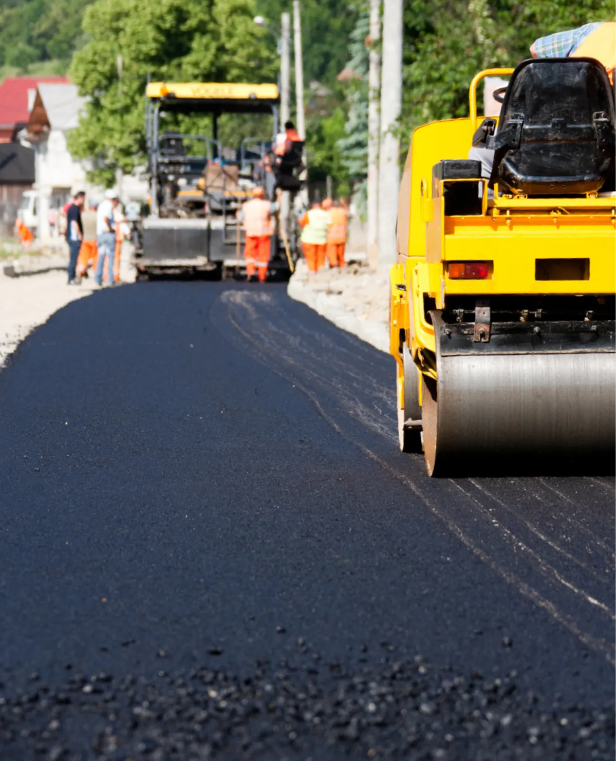 Workers and machinery paving a new asphalt road on a sunny day in a residential area.
