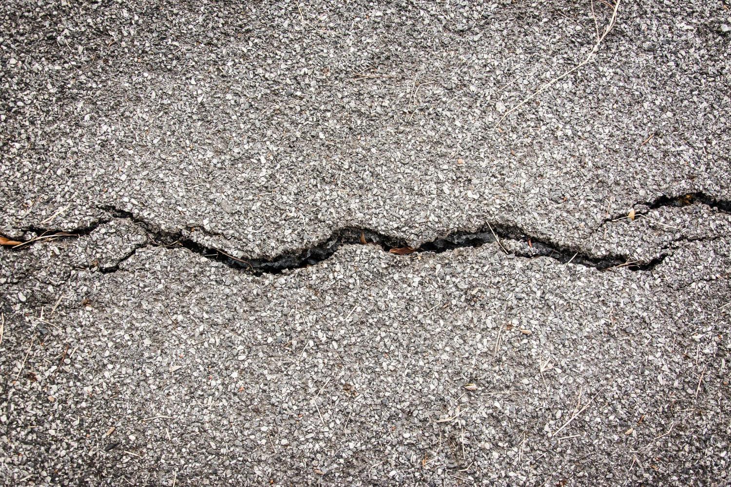 A close-up of a cracked pavement surface, showing a jagged line running horizontally across the asphalt.
